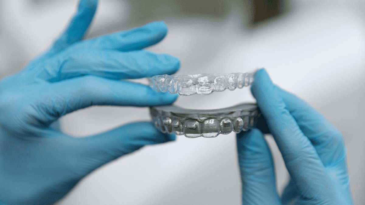 Gloved hands comparing a clear aligner with a bracket model